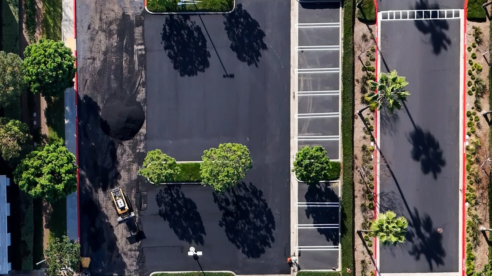 Aerial view of a commercial parking lot with concrete curbs and landscaped islands during paving work